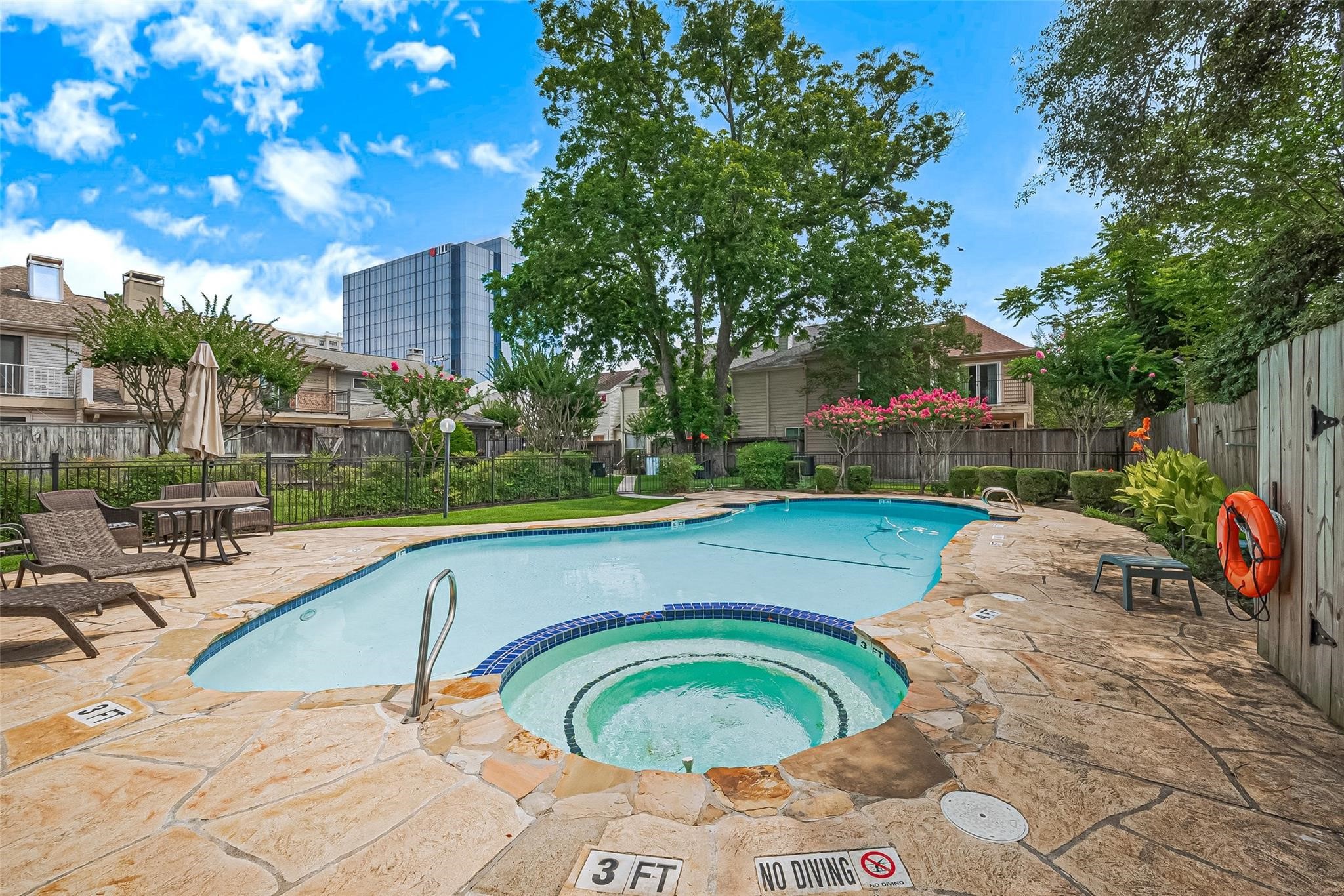 4305 Westheimer Road Houston, TX 77027 - Photo 24 of 25 Welcome to the community pool; refreshing swimming pool with attached hot tub, surrounded by a stone patio. The area is landscaped with trees and shrubs, providing a serene outdoor space for relaxation and entertainment.