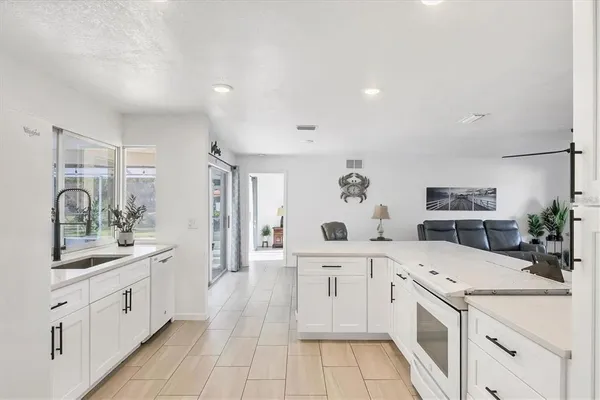 a large white kitchen with a stove a sink dishwasher and a refrigerator with wooden floor