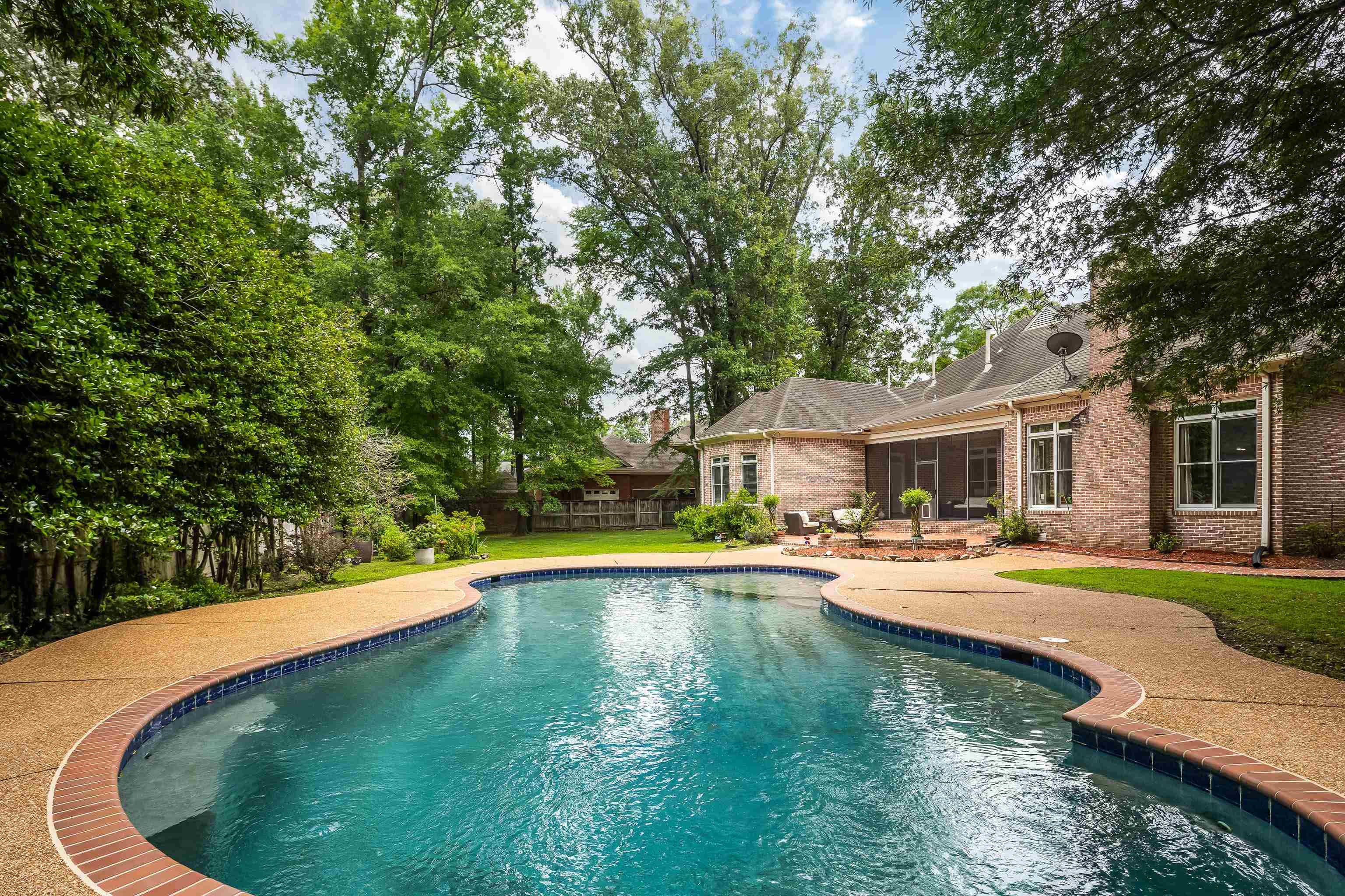 Curved swimming pool featuring a tile edge, brick coping, and a surrounding aggregate deck