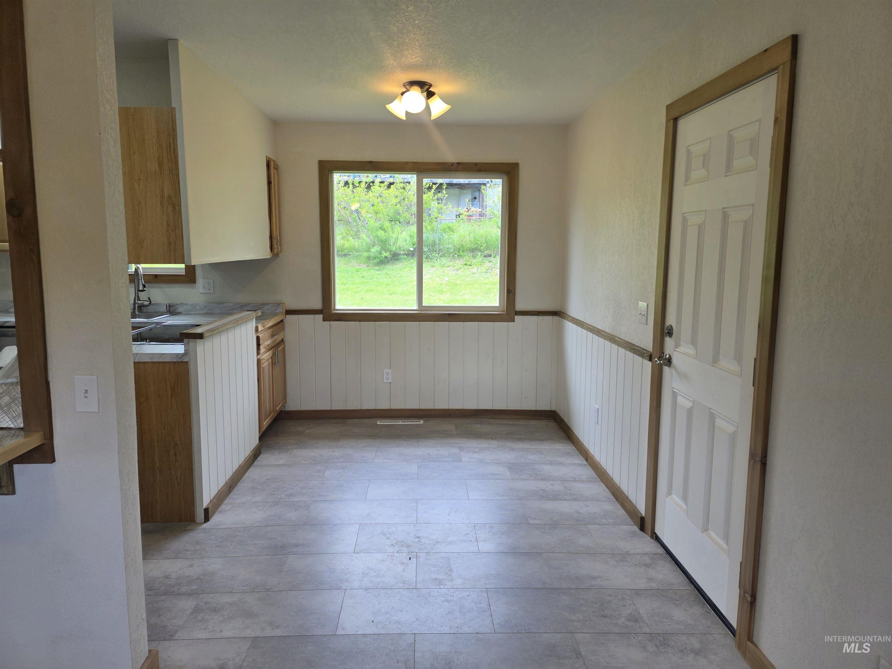 310 Fir Road Kamiah, ID 83536 - Photo 15 of 32 Kitchen and dining area featuring wood-finish cabinetry, a window with natural light, textured wall paneling, and tile flooring