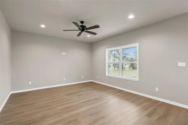an empty room with wooden floor fan and windows