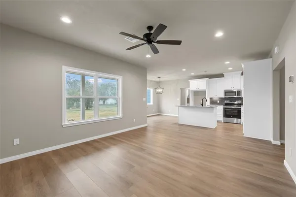 a view of an empty room and kitchen with wooden floor and a window