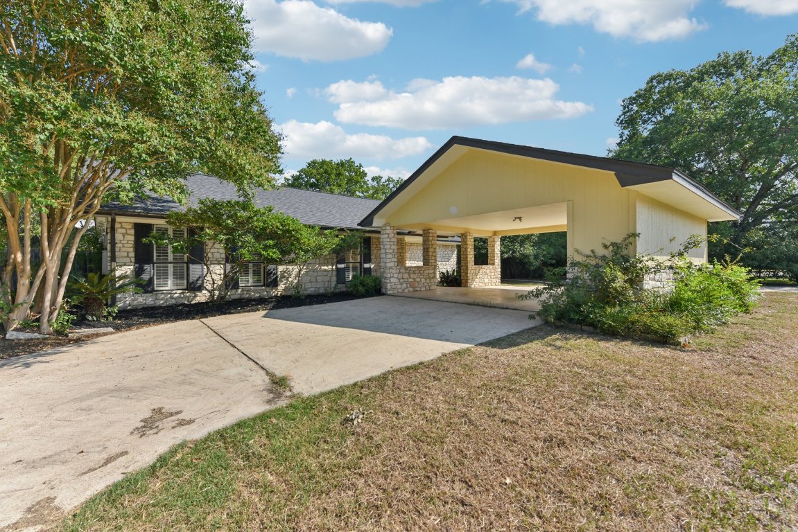 Back of house featuring stone siding, concrete driveway, a lawn, and roof with shingles