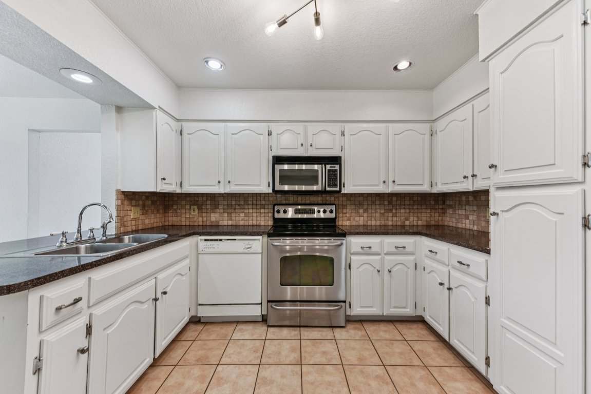 503 Hackberry Street Lockhart, TX 78644 - Photo 18 of 36 Kitchen with appliances with stainless steel finishes, light tile patterned floors, white cabinets, tasteful backsplash, and a textured ceiling