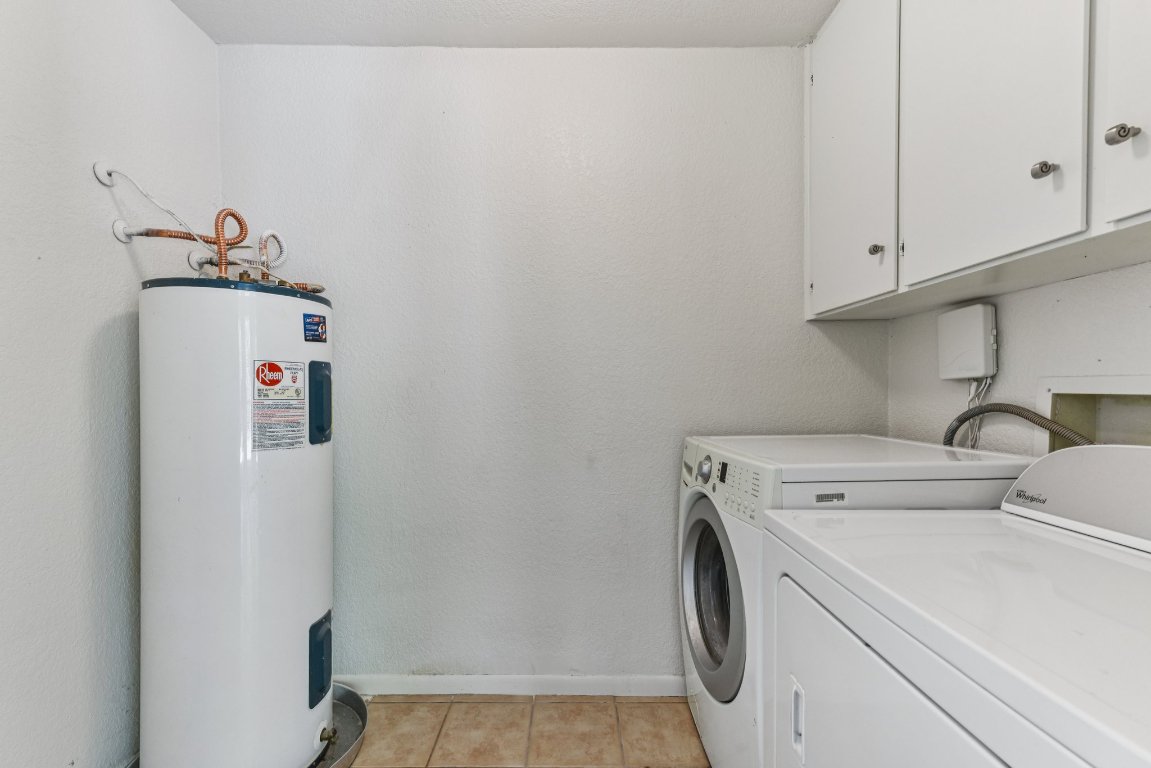 503 Hackberry Street Lockhart, TX 78644 - Photo 22 of 36 Laundry room with light tile patterned flooring, water heater, washing machine and dryer, and cabinet space