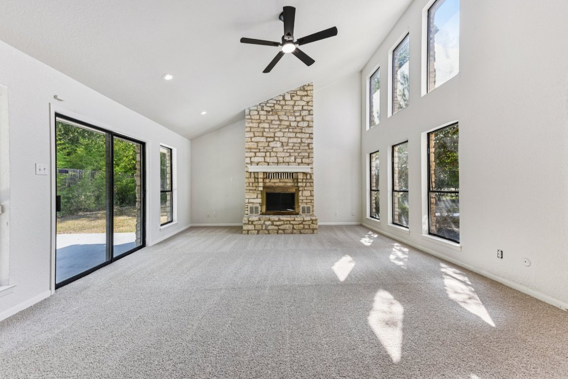 503 Hackberry Street Lockhart, TX 78644 - Photo 3 of 36 Unfurnished living room with carpet flooring, high vaulted ceiling, a stone fireplace, a ceiling fan, and healthy amount of natural light