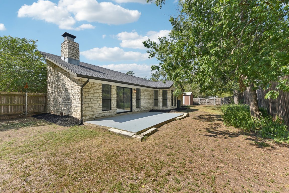 503 Hackberry Street Lockhart, TX 78644 - Photo 8 of 36 Back of property featuring a fenced backyard, stone siding, a patio area, a chimney, and a shingled roof