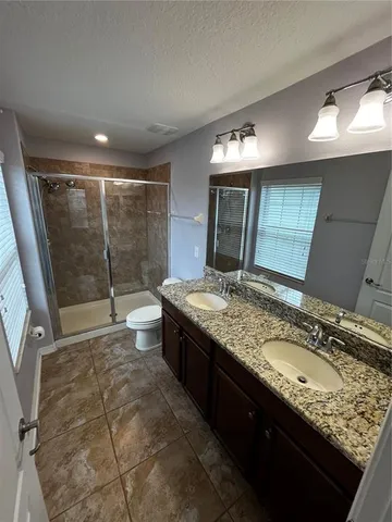 a bathroom with a granite countertop sink a toilet a mirror and shower
