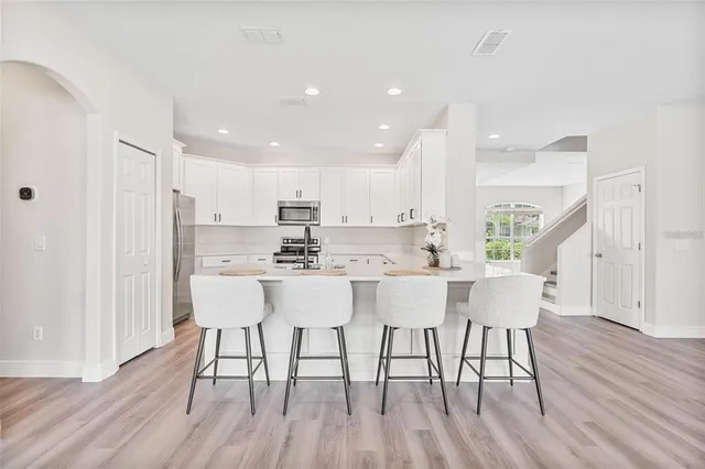 a kitchen with stainless steel appliances granite countertop a dining table chairs wooden floors and white cabinets