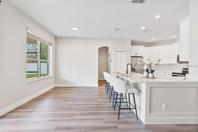 a kitchen with stainless steel appliances a sink a stove a refrigerator cabinets and a dining table with wooden floor