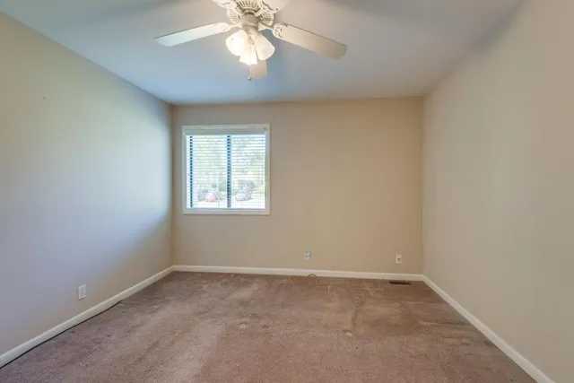 an empty room with a chandelier fan and windows