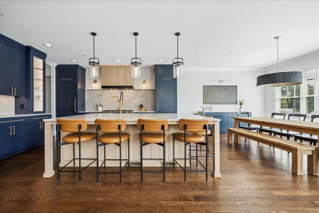 a kitchen with stainless steel appliances granite countertop a stove top oven a sink a dining table and chairs with wooden floor