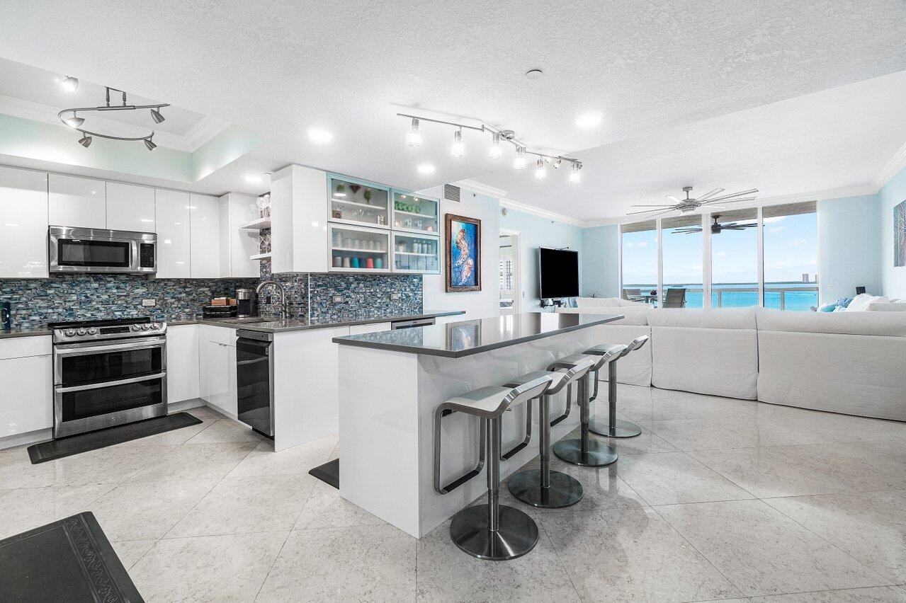 2650 Lake Shore Drive, Unit 701 Riviera Beach, FL 33404 - Photo 11 of 64 a kitchen with stainless steel appliances kitchen island granite countertop a stove top oven a sink a dining table and chairs