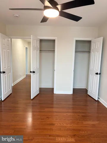 a view of an empty room with wooden floor and a ceiling fan