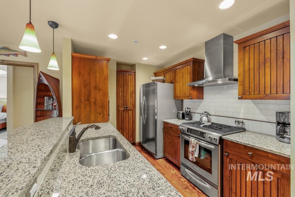 616 North 3rd Street, Unit 304 McCall, ID 83638 - Photo 21 of 38 Kitchen with appliances with stainless steel finishes, wall chimney exhaust hood, pendant lighting, light stone countertops, and light wood-style floors