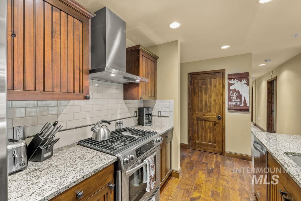 616 North 3rd Street, Unit 304 McCall, ID 83638 - Photo 22 of 38 Kitchen with stainless steel appliances, wall chimney exhaust hood, light stone counters, dark wood finished floors, and recessed lighting