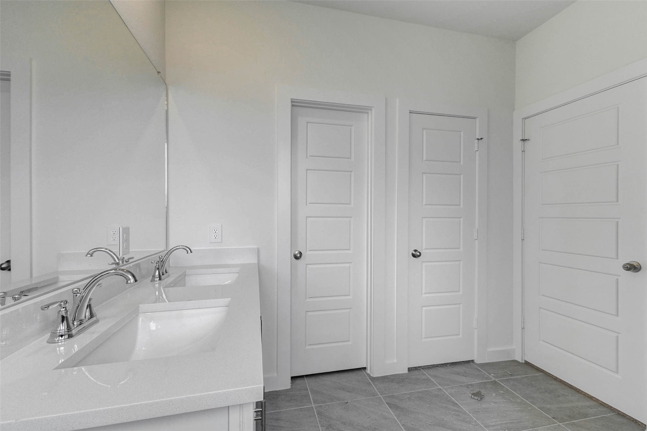 6471 Escondido Drive Rosharon, TX 77583 - Photo 22 of 33 Primary bath vanity area featuring dual undermount sinks, quartz-style countertop, chrome faucets, large mirror, tile flooring, and nearby doorways for closet and bath access. The bright white cabinetry and neutral finishes create a clean, functional space for everyday routines.