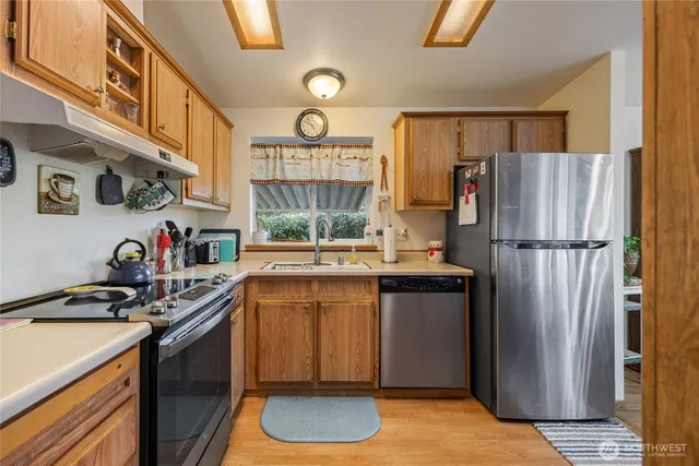 a kitchen with stainless steel appliances granite countertop a refrigerator a sink dishwasher a stove and a dining table with wooden floor