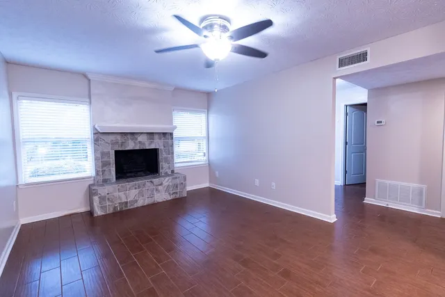 an empty room with windows a fireplace a ceiling fan and wooden floor