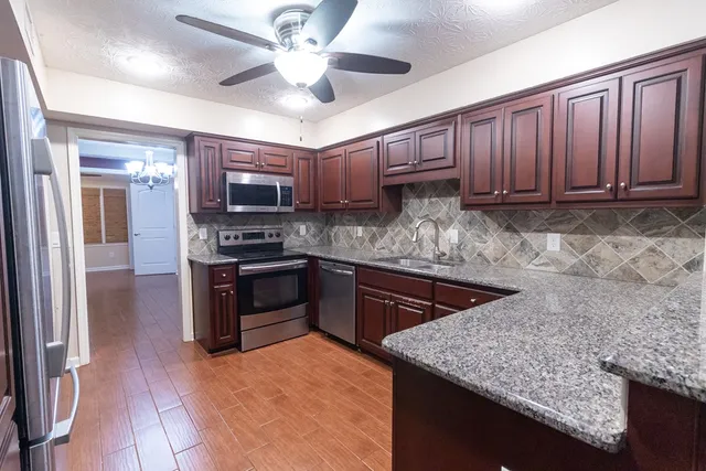 a kitchen with stainless steel appliances granite countertop a sink dishwasher stove and refrigerator with wooden floor