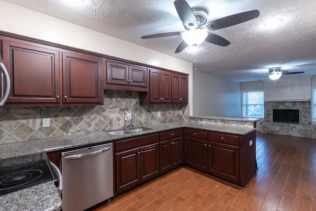 a kitchen with stainless steel appliances granite countertop wooden cabinets a sink dishwasher a stove and a refrigerator with wooden floor