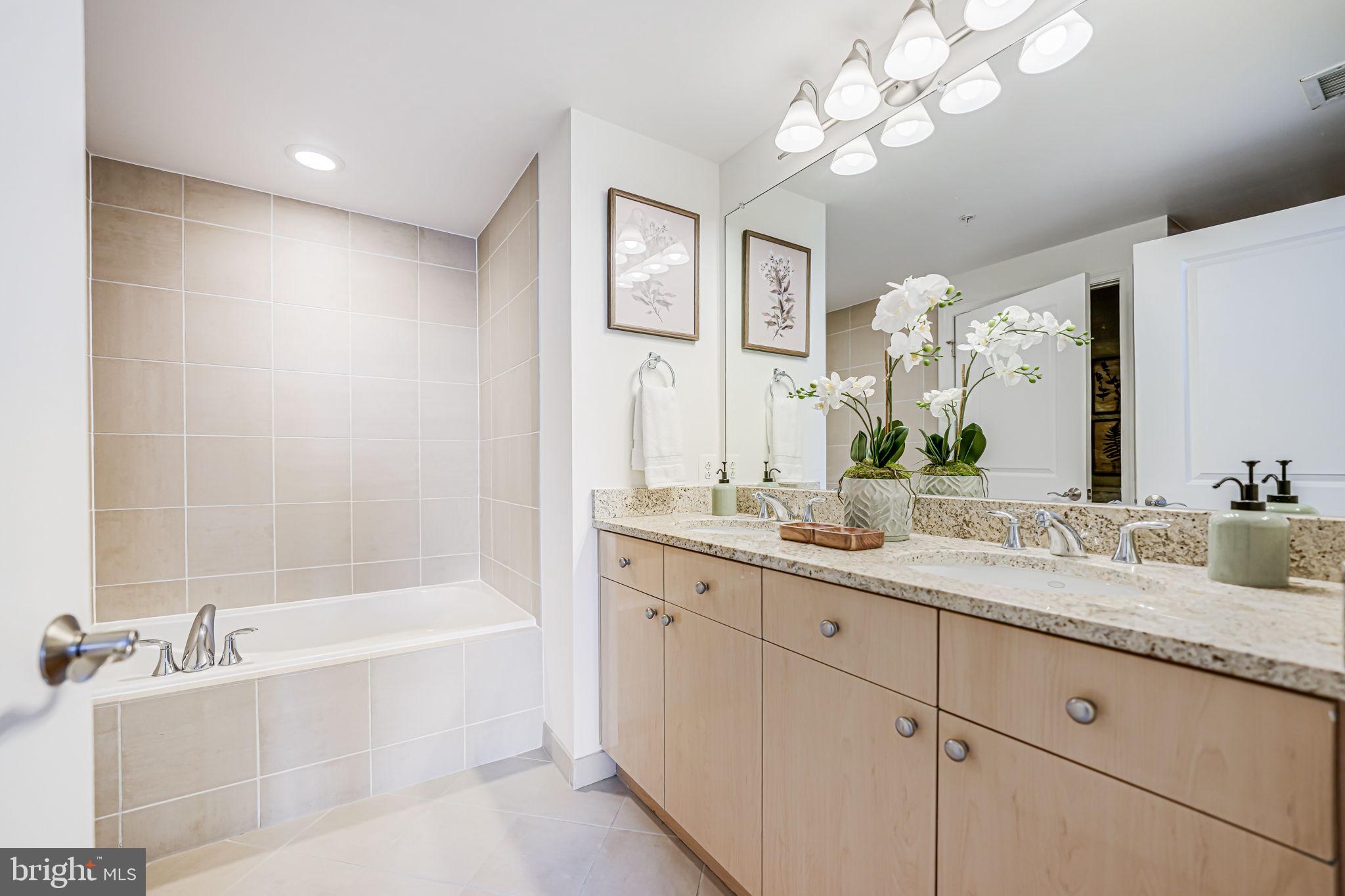 11990 Market Street, Unit 413 Reston, VA 20190 - Photo 23 of 82 a bathroom with a granite countertop sink a large mirror and a bathtub with shower