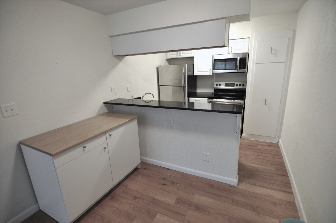2207 Leon Street, Unit 201 Austin, TX 78705 - Photo 2 of 10 Kitchen with white cabinetry, stainless steel appliances, a peninsula, dark wood-type flooring, and dark countertops