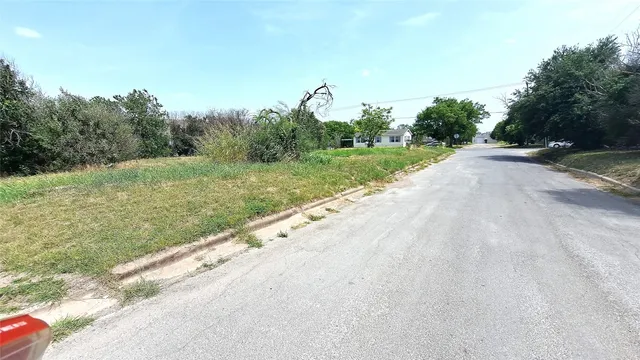a view of a road with a yard and large trees