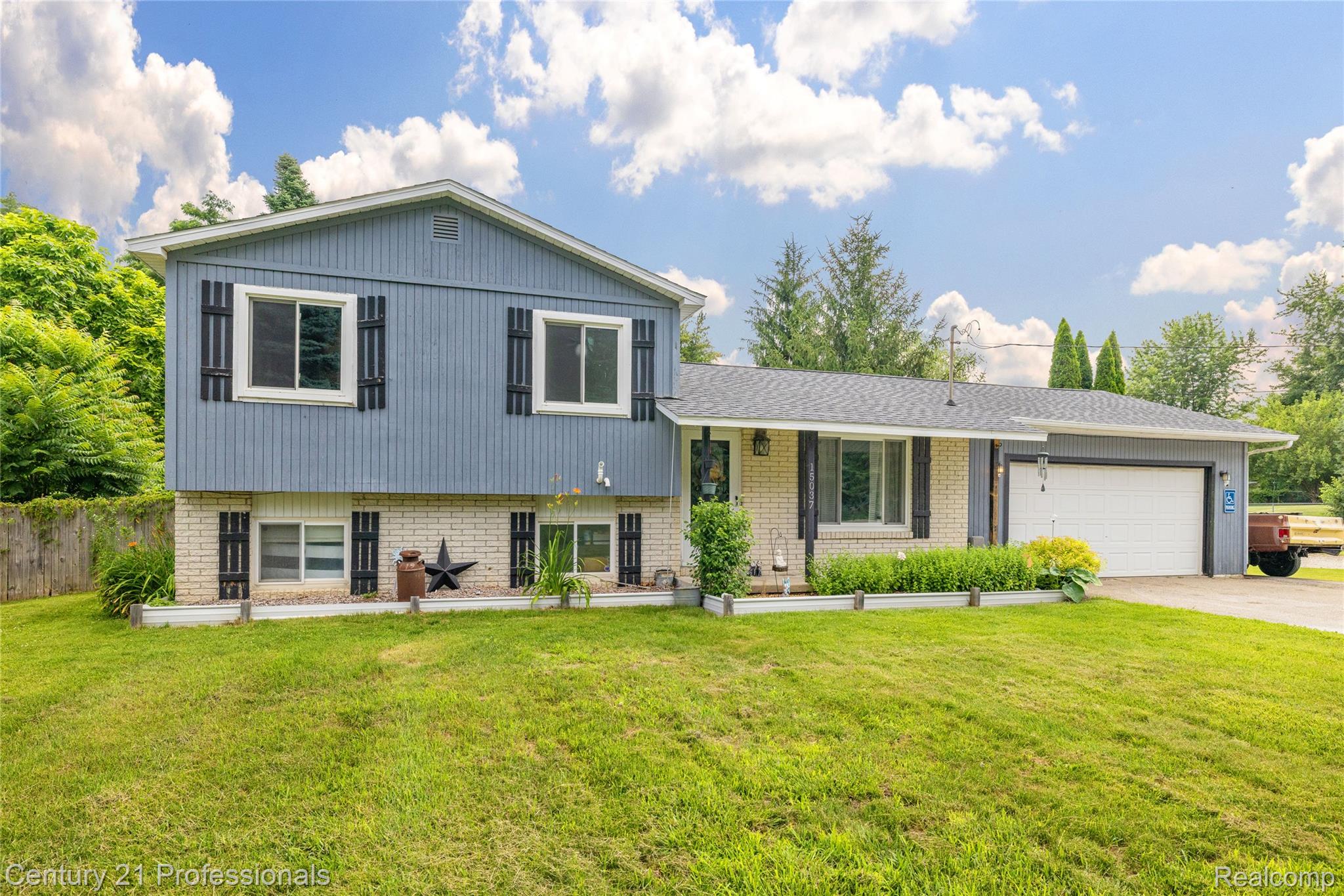 15037 Hogan Road Linden, MI 48451 - Photo 1 of 38 Split-level residence featuring a two-car garage, light-toned brick facade, and blue vertical siding