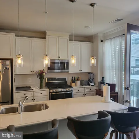 a kitchen with stainless steel appliances a stove a sink a microwave a refrigerator and white cabinets with wooden floor