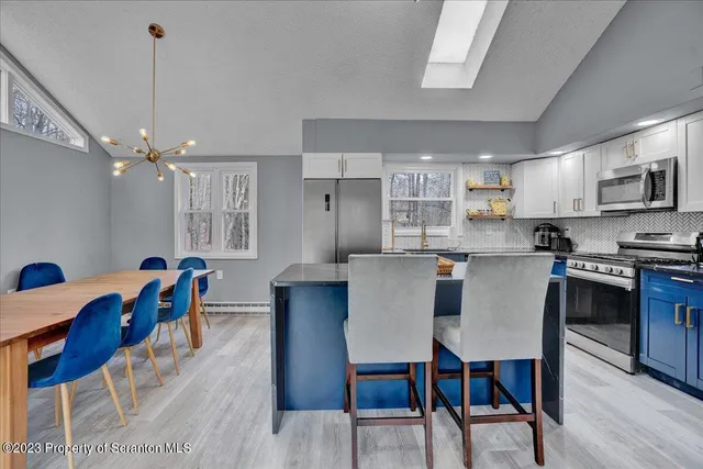 a kitchen with stainless steel appliances kitchen island granite countertop a dining table chairs and a refrigerator