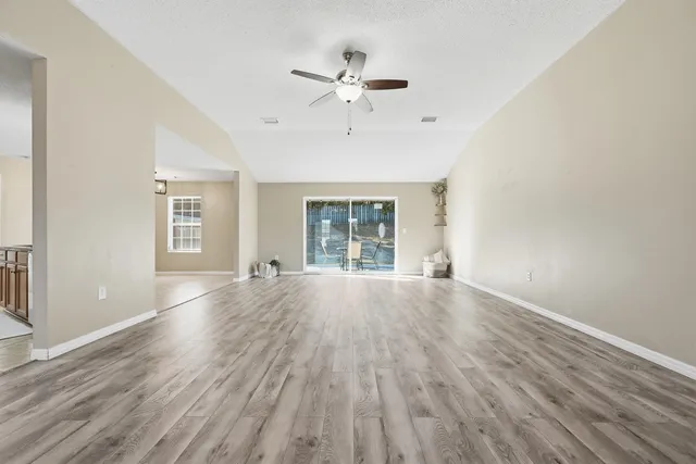 a view of an room with wooden floor ceiling fan and windows