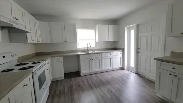 a kitchen with granite countertop a sink a stove cabinets and wooden floor