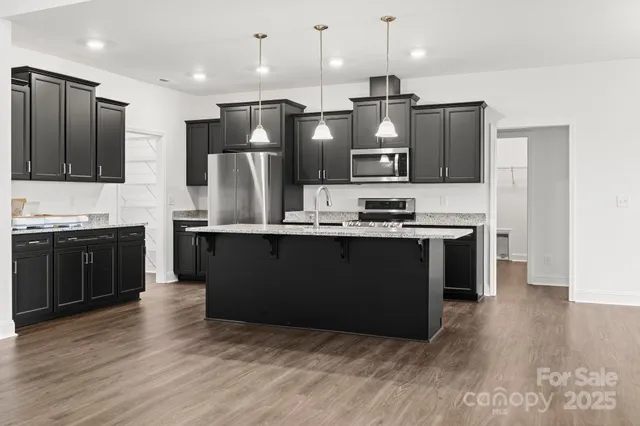 a kitchen with stainless steel appliances kitchen island granite countertop a refrigerator a sink a stove and oven with wooden floor