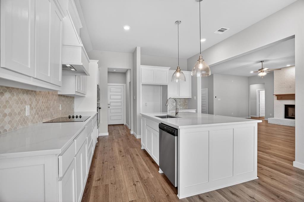 504 Clifton Court Springtown, TX 76082 - Photo 13 of 36 Modern kitchen featuring white shaker cabinetry, light-toned patterned backsplash, a central island with integrated sink, and wood-finish flooring