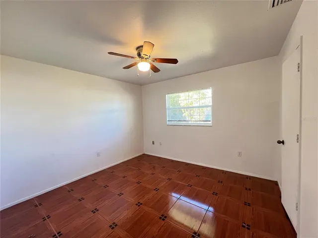 a view of an empty room with wooden floor and a ceiling fan
