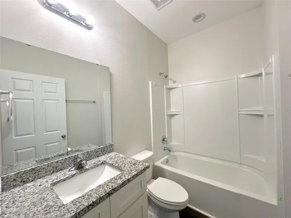 a bathroom with a granite countertop bathtub shower sink vanity mirror and toilet
