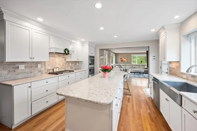a large kitchen with granite countertop a sink dishwasher stove and white cabinets with wooden floor