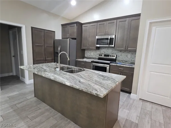 a kitchen with kitchen island granite countertop stainless steel appliances stove microwave refrigerator and sink