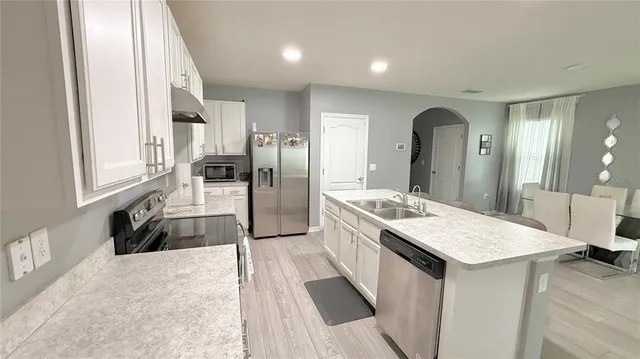 a kitchen with a table chairs a sink dishwasher a refrigerator and cabinets with wooden floor