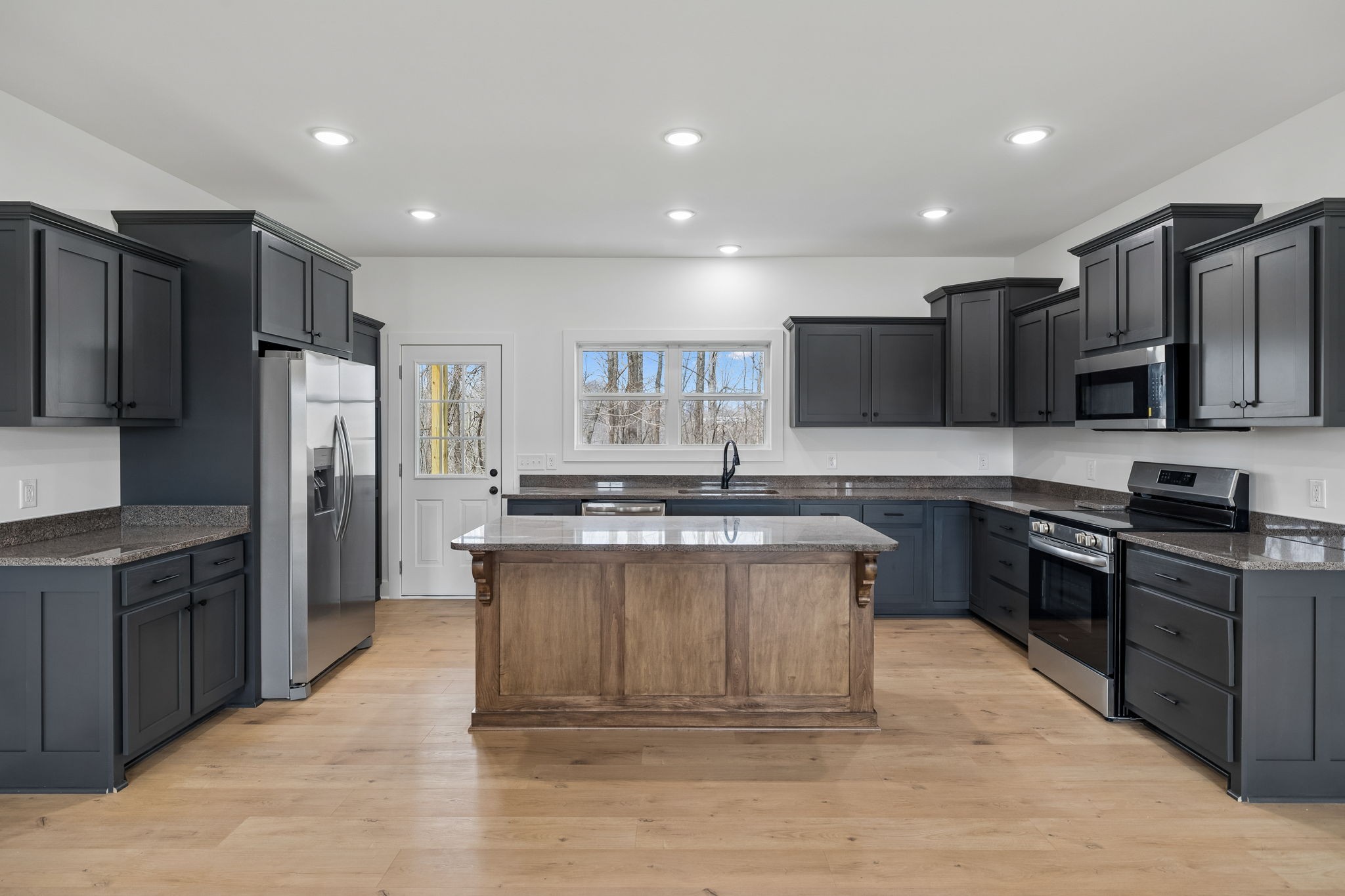a large kitchen with stainless steel appliances kitchen island granite countertop a stove a refrigerator a sink a microwave and wooden cabinets