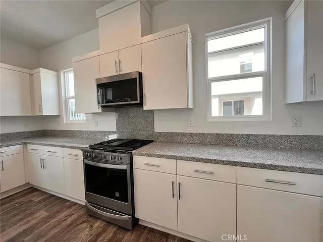 a kitchen with granite countertop white cabinets appliances and a window