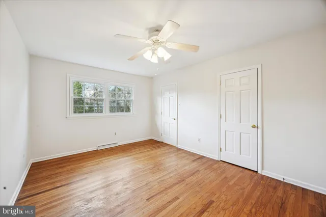 an empty room with wooden floor closet and windows fan