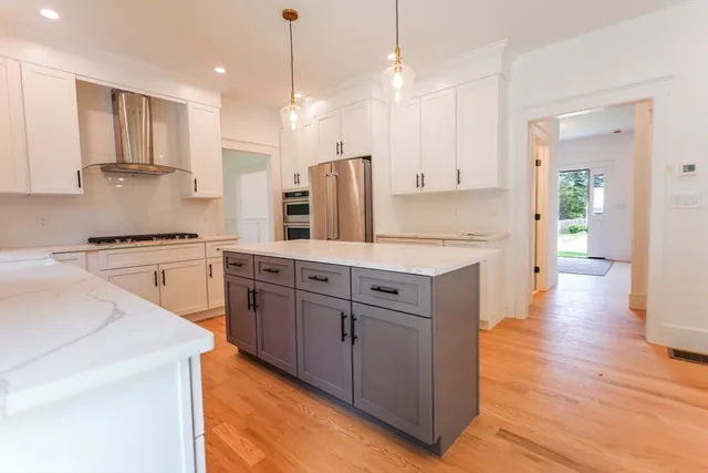 a kitchen with stainless steel appliances granite countertop a refrigerator a sink dishwasher a stove and white countertops with wooden floor