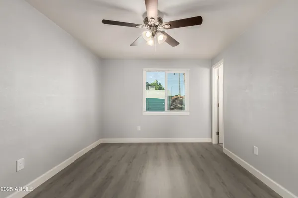 an empty room with wooden floor chandelier fan and windows