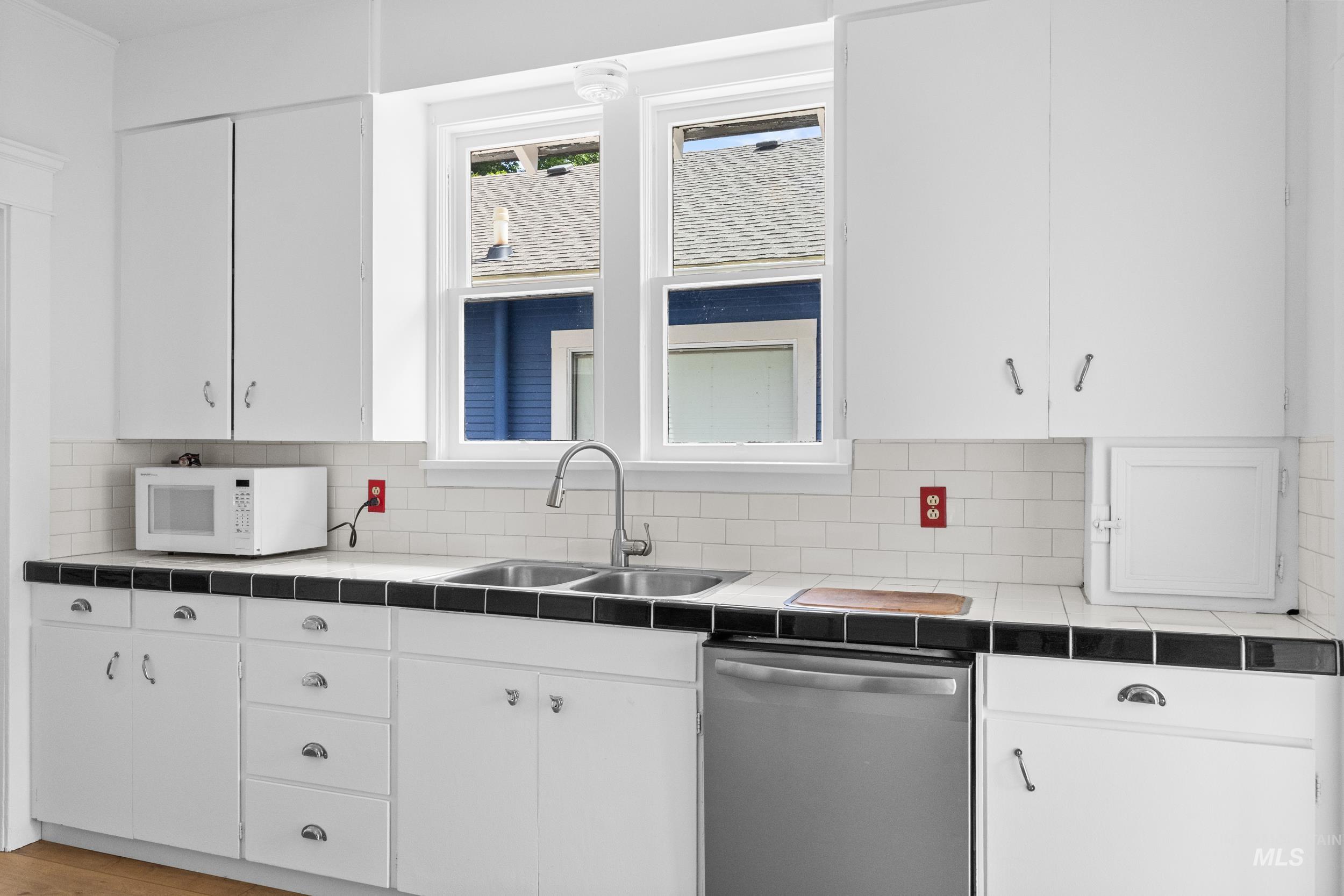 2119 West Brumback Street Boise, ID 83702 - Photo 13 of 30 Kitchen featuring white cabinetry, a double basin stainless steel sink, a stainless steel dishwasher, black tile countertops, and a white subway tile backsplash