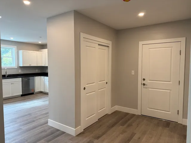 an empty room with wooden floor kitchen view and a window