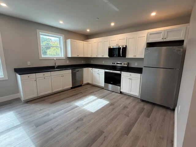 a kitchen with granite countertop a refrigerator a sink a stove a microwave and wooden floor