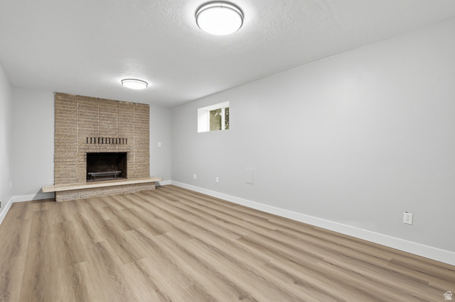 629 King Circle Layton, UT 84041 - Photo 15 of 26 Spacious room featuring a brick fireplace with a stone hearth, light wood-finish flooring, white baseboards, and neutral wall tones