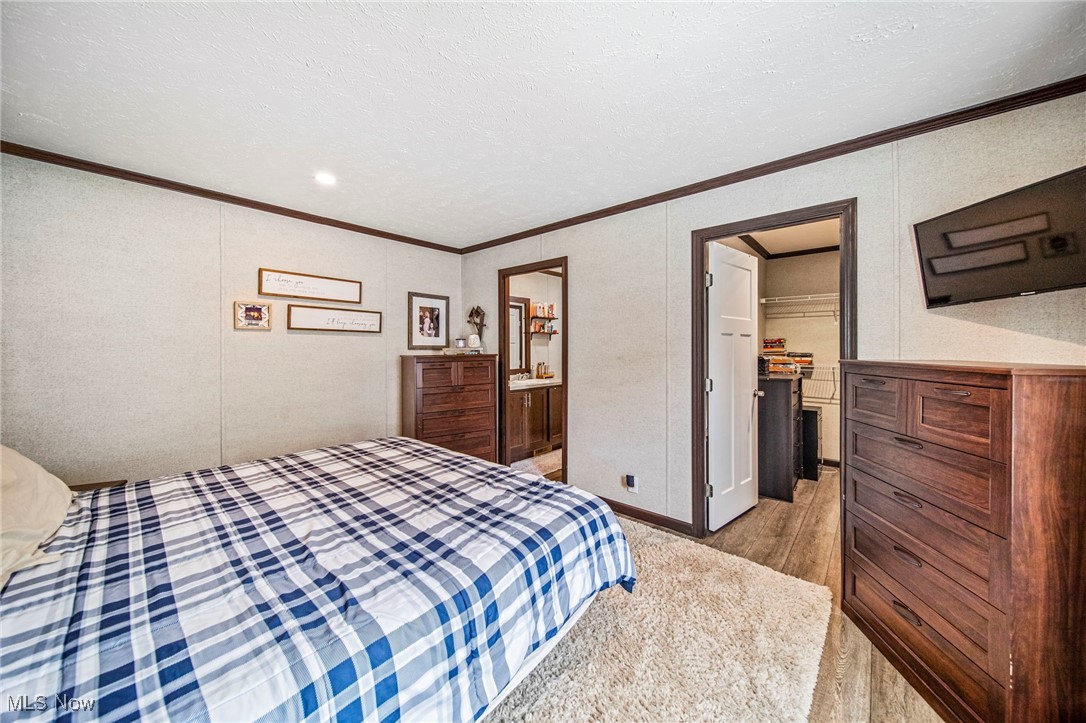 202 West Main Road, Unit LOT 13 Conneaut, OH 44030 - Photo 19 of 23 Bedroom with a walk in closet, ornamental molding, light wood-style floors, connected bathroom, and a textured ceiling